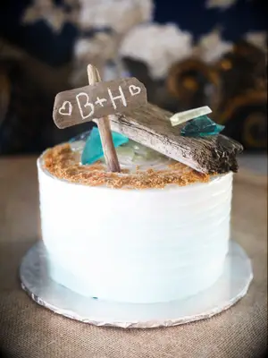 Small one-tier beach wedding cake with sandy top and custom cake topper