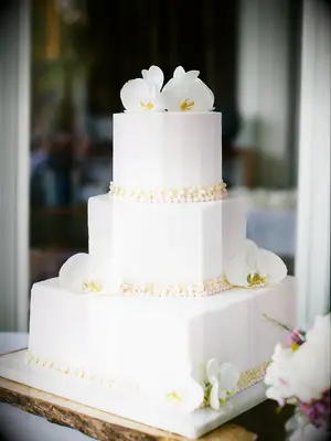 Three-tier white beach wedding cake with tropical orchid florals