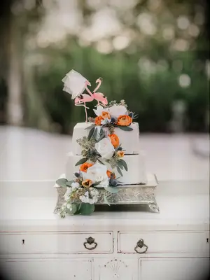 Three-tier square beach wedding cake with oranges and flamingo topper
