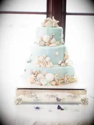 Three-tier light blue beach-themed wedding cake with seashells and starfish