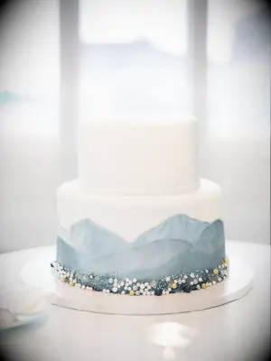 Small white beach-themed wedding cake with blue watercolor base and sea glass gem accents