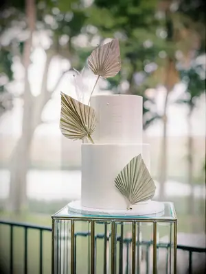 Trendy beach wedding cake with two white tiers and pressed gold palms