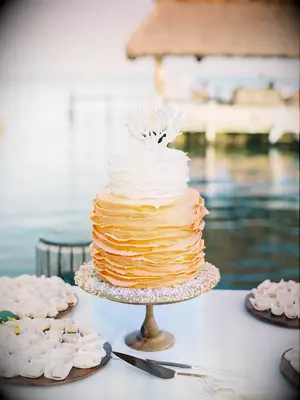 Orange and white ruffled beach wedding cake with coral topper