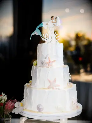 White beach-themed wedding cake with custom mermaid cake topper