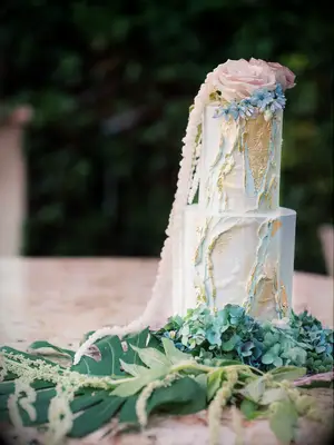 Ethereal blue and gold beach wedding cake on bed of greenery