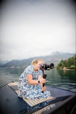 A videographer sits on the bow of a boat so she can capture the best shot.