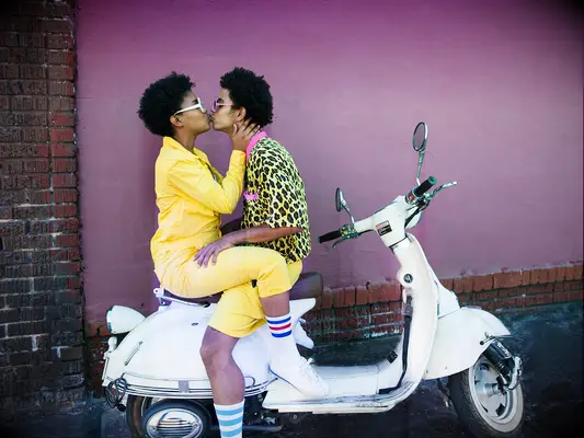 A couple kiss on the back of a Vespa.
