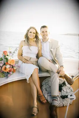 Couple Poses: Couple sits on the bow of a sailboat while smiling at the camera. 