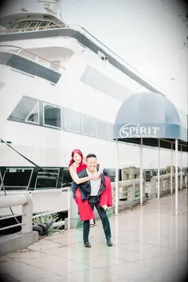 Cute Couple Poses: Wife poses on her husbands back with a large boat in the background. 