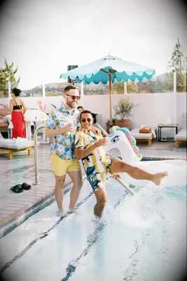 Cute Couple Poses: Couple splashes in the pool while smiling at the camera. 