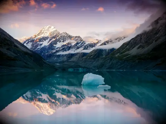 Snowcapped peak of mount Cook reflecting in still lake with iceberg at sunset in New Zealand