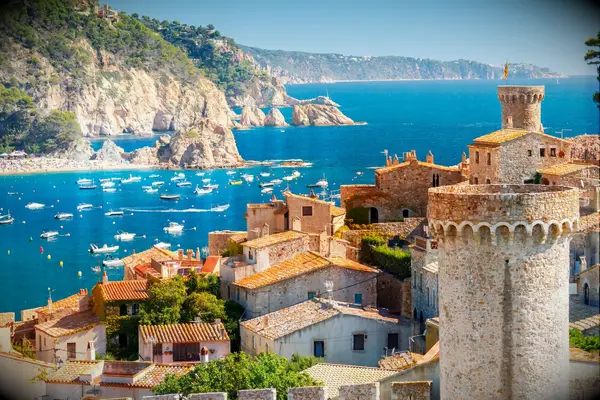 View of the Costa Brava coastline that features beautiful historic buildings and a sparkling ocean. 